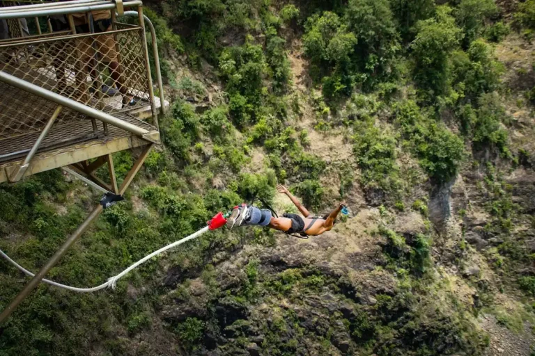 View from bridge of person in mid air with bungy rope on their ankles diving into the gorge below