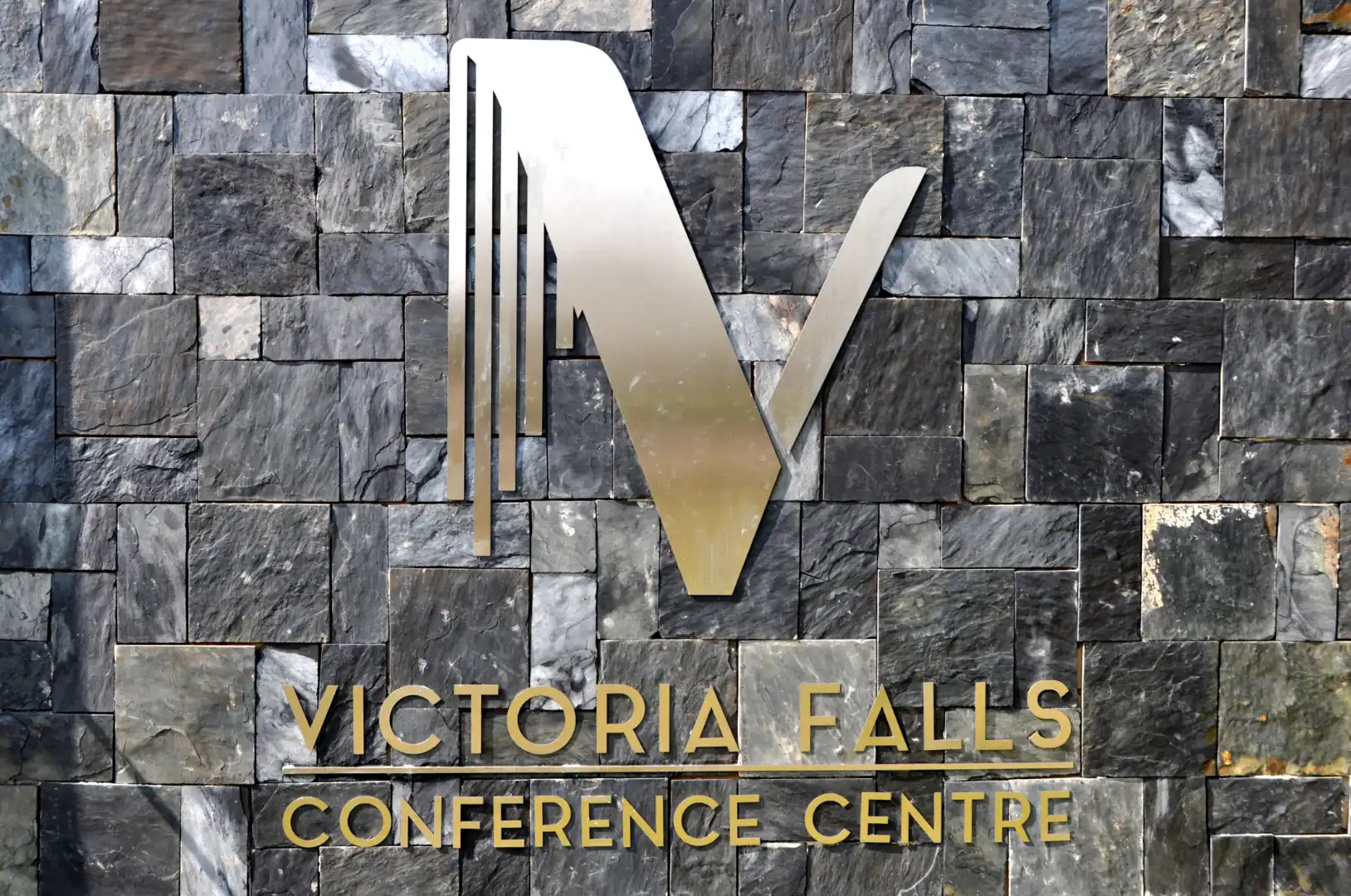 Lodge logo on a stone wall and gold writing below: Victoria Falls Conference centre