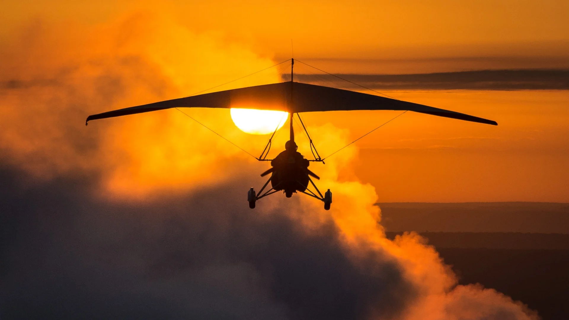Microlight flying into the sunset with clouds being lit of by the red sun