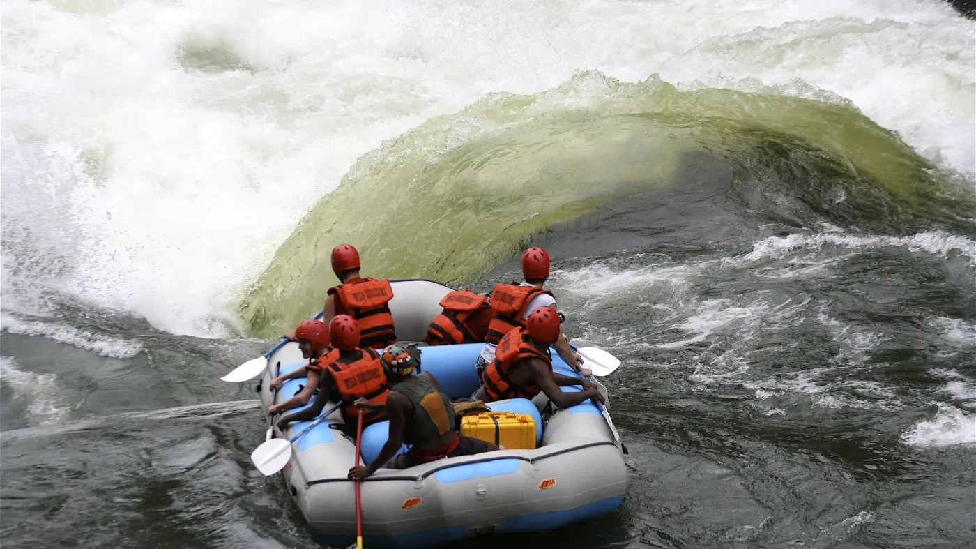 Raft with adventure seekers dressed in red helmuts and life jackets about to go through a gorge with angry looking water around it